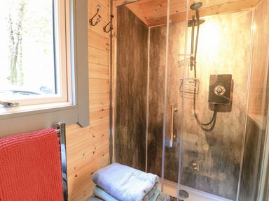 A bathroom with a glass shower enclosure wooden wall paneling a window and folded towels at Elleric Pods - The Last Resort Fasnacloich near Appin
