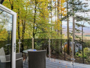A balcony with wicker chairs and a glass table overlooking a forest with autumn leaves at Elleric Pods - The Last Resort Fasnacloich near Appin