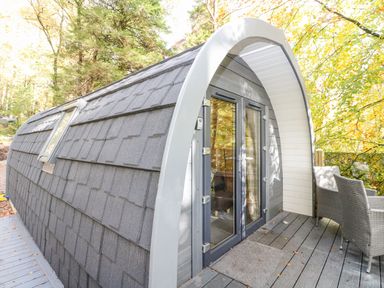 A small pod-like cabin with glass double doors and two chairs on a wooden deck surrounded by trees at Elleric Pods - The Last Resort Fasnacloich near Appin