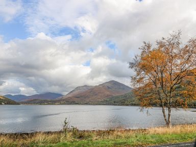 A lake with hills in the background and a tree with orange leaves by the shore at Elleric Pods - The Last Resort in Fasnacloich near Appin