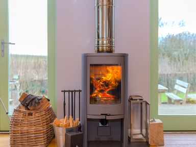 A wood burning stove with fire inside and firewood beside it in a room with glass doors at Smugglers Bodmin Moor St Breward near St Tudy