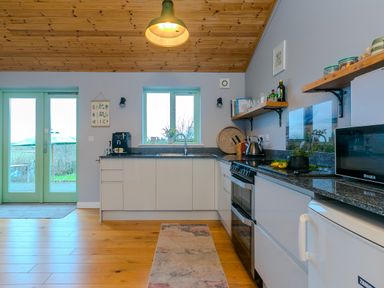 A kitchen with white cabinets and wooden ceiling at Smugglers in Bodmin Moor St Breward near St Tudy