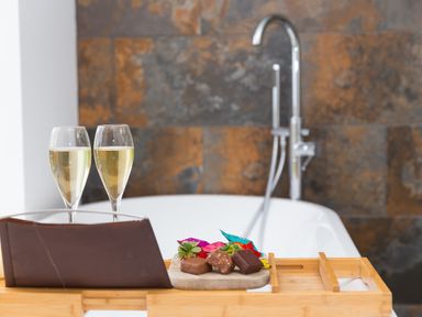 A bathroom with a bathtub featuring a wooden tray holding two glasses of champagne and chocolates at Smugglers in Bodmin Moor St Breward near St Tudy