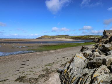 A sandy beach with rocks on the side and a stone house near the shoreline at Min-Y-Ffordd in Dinas Cross