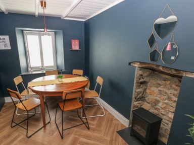 A dining area with a wooden table and six chairs near a window and a stone fireplace with mirrors on the wall at Min-Y-Ffordd in Dinas Cross