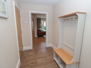 A hallway with wooden floor tiles a wooden door a coat rack with hooks and storage and a view into a living room at Breamish in Christon Bank near Embleton