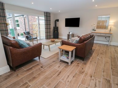 A living room with two leather sofas a wooden coffee table and a TV on the wall at Breamish in Christon Bank near Embleton
