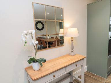 A wooden table with a white flower pot and a lamp under a wall mirror showing dining chairs at Breamish Christon Bank near Embleton