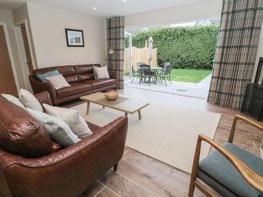 A living room with brown leather sofas, cushions, a wooden coffee table, and patio doors opening to a garden at Breamish Christon Bank near Embleton