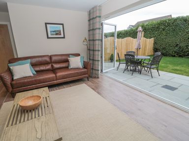 A living room with a brown leather sofa and coffee table opening to a patio with a table and chairs at Breamish Christon Bank near Embleton