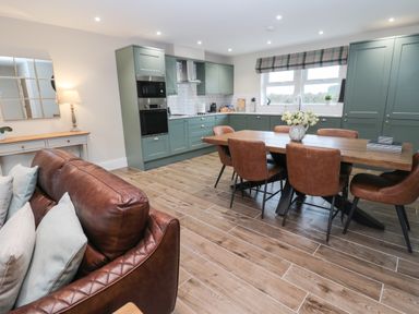 A kitchen and dining area with green cabinets wooden dining table and brown leather chairs at Breamish in Christon Bank near Embleton