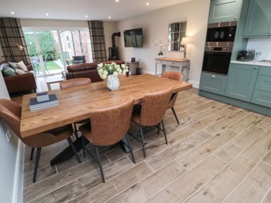 A dining area with a wooden table and brown chairs adjacent to a kitchen with green cabinets and built-in ovens in a living space at Breamish Christon Bank near Embleton