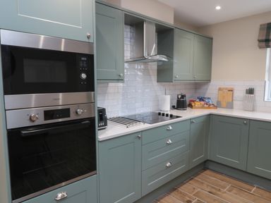 A kitchen with green cabinets a built-in oven and microwave a cooktop and countertop appliances at Breamish Christon Bank near Embleton