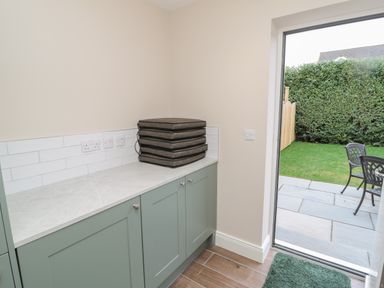 A room with green cabinets and cushions on the countertop next to a door opening to a garden with patio furniture at Breamish in Christon Bank near Embleton