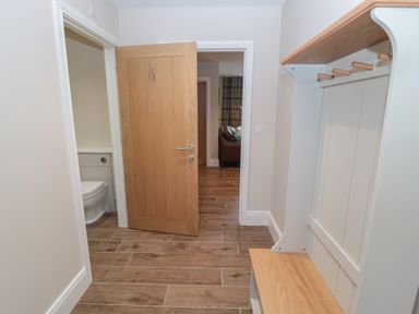 An entryway with a wooden door open to a toilet and a hallway with a brown couch at Breamish Christon Bank near Embleton