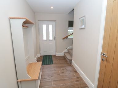 A hallway with a wooden bench and coat rack near the entrance door and carpeted stairs at Breamish in Christon Bank near Embleton