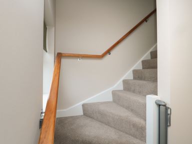 A carpeted staircase with a wooden handrail and a safety gate at the bottom at Breamish Christon Bank near Embleton