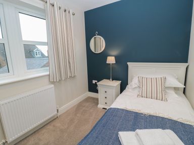 A bedroom with a single bed bedside table lamp round mirror and window at Breamish Christon Bank near Embleton