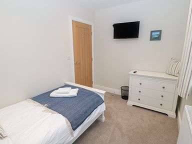 A bedroom with a single bed covered by a blue blanket and white towels a white dresser with a pillow a wall-mounted TV and a wooden door at Breamish Christon Bank near Embleton