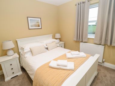 A bedroom with a double bed two bedside tables with lamps and a window with curtains at Breamish in Christon Bank near Embleton