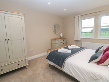 A bedroom with a bed pillows folded towels a wardrobe chest of drawers and two windows at Breamish in Christon Bank near Embleton