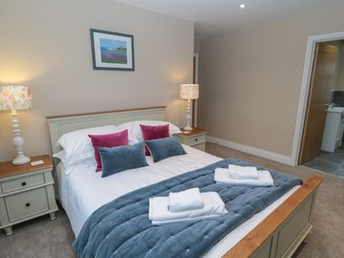 A bedroom with a bed with pillows and blankets two bedside tables with lamps and a door leading to a bathroom at Breamish in Christon Bank near Embleton
