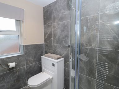 A bathroom with a toilet a shower with glass door gray tiled walls and a window with a blind at Breamish Christon Bank near Embleton