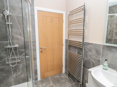 A bathroom with a wooden door a glass shower enclosure a chrome towel radiator and a sink with soap at Breamish Christon Bank near Embleton
