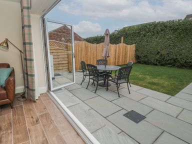 A patio with a round table and four chairs next to a lawn and wooden fence at Breamish in Christon Bank near Embleton