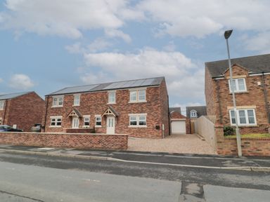 A semi detached brick house with solar panels on the roof and a gravel driveway at Breamish in Christon Bank near Embleton
