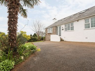 The exterior of a white house with stone detail and multiple windows with a driveway and plants including a palm tree at The Palms in Abersoch