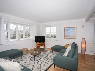 A living room with green sofas a TV on a wooden stand and framed beach painting at The Palms in Abersoch