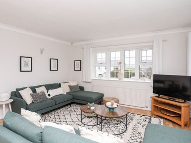 A living room with green sofas a wooden coffee table a patterned rug a TV on a wooden stand and framed pictures on the wall at The Palms in Abersoch