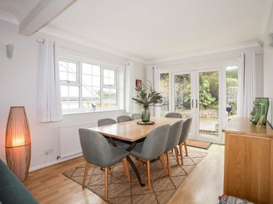 A dining room with a wooden table surrounded by eight chairs a wooden cabinet a lamp and glass doors at The Palms in Abersoch