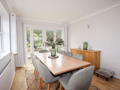 A dining room with a wooden table surrounded by gray chairs and a sideboard with decorations at The Palms in Abersoch