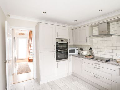 A kitchen with white cabinets built in oven microwave toaster and stovetop at The Palms in Abersoch