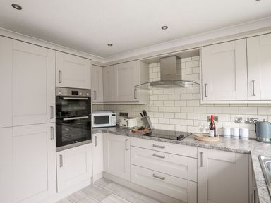 A kitchen with white cabinets a built-in oven microwave toaster stovetop and kettle at The Palms in Abersoch