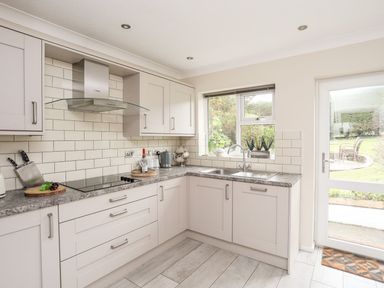 A kitchen with grey cabinets a window double sink and glass door to garden at The Palms in Abersoch