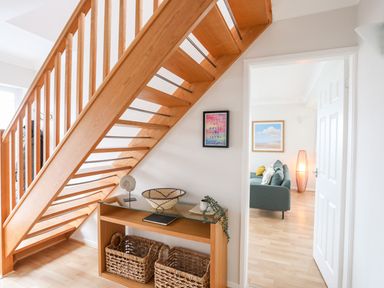 A wooden staircase above a table with baskets and decorative items next to a doorway showing a room with a sofa and lamp at The Palms in Abersoch