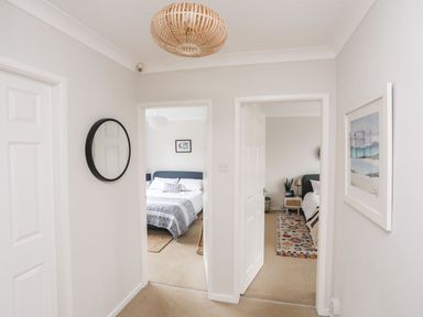A hallway with two open doors leading to bedrooms a round wall mirror and a framed picture on the walls at The Palms in Abersoch