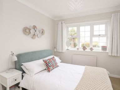 A bedroom with a double bed white bedding and a colorful pillow two bedside tables with lamps and a window with white curtains