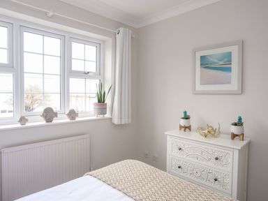 A bedroom corner with a textured chest of drawers holding two small plants and a decorative item next to a window with three fish ornaments on the sill at The Palms in Abersoch