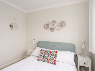 A bedroom with a double bed white bedding a colorful pillow two bedside tables with lamps a wall mirror and decorative wall art at The Palms in Abersoch