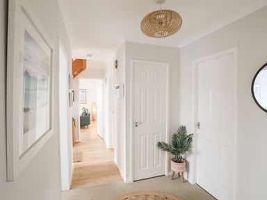 A hallway with white doors a potted plant on a stand and a round mirror at The Palms in Abersoch