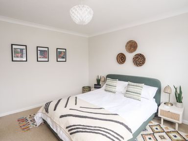 A bedroom with a green upholstered bed white bedding patterned pillows and wall art at The Palms in Abersoch