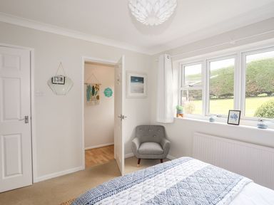 A bedroom with a gray armchair near a window and a bed with a patterned blanket at The Palms in Abersoch