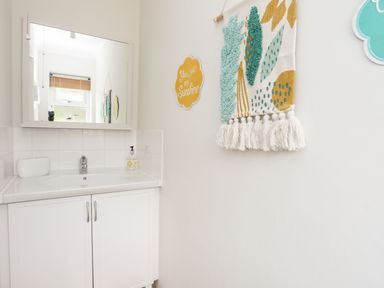 A bathroom sink with a mirror above and decorative wall hangings at The Palms in Abersoch
