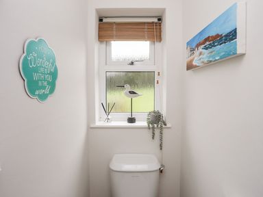 A small bathroom with a toilet under a window with a wooden blind and decorations on the windowsill at The Palms in Abersoch