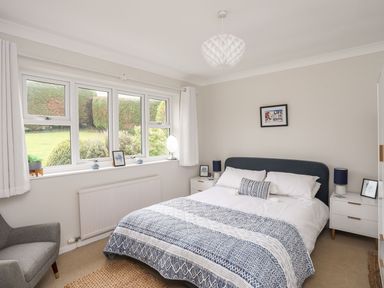 A bedroom with a double bed and blue patterned bedding near a window with white curtains at The Palms in Abersoch