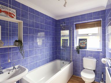 A bathroom with a white bathtub shower toilet and sink with blue tiled walls and a window at The Palms in Abersoch
